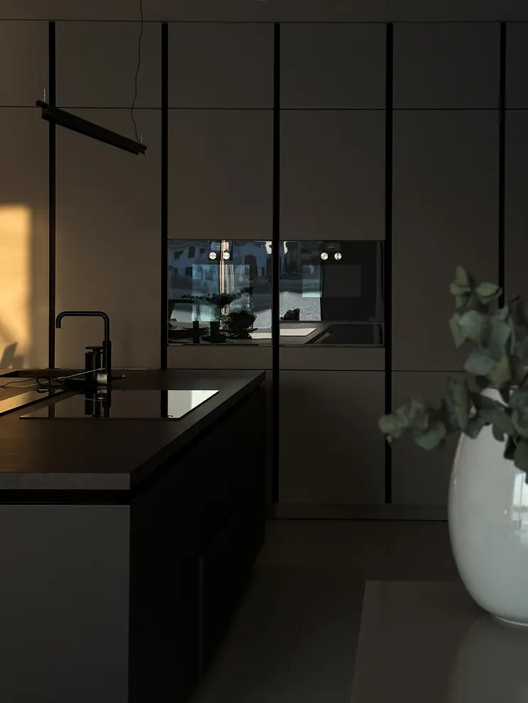 Kitchen island with a black tap and tall graphite cabinets in evening light