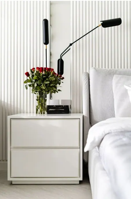 White lacquered bedside table against fluted panels with black articulated wall lamps