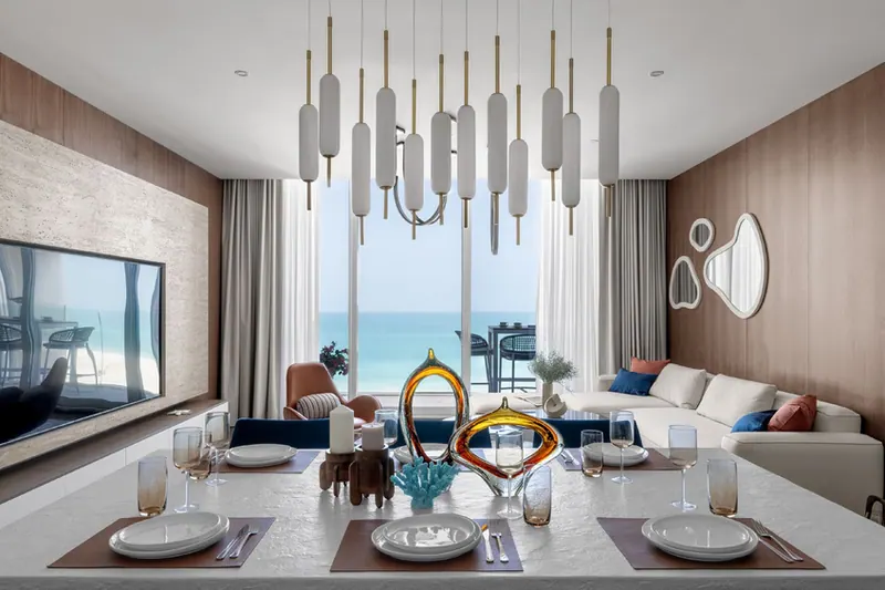 Dining table set for guests under a cluster of opal glass pendants, with the sea behind